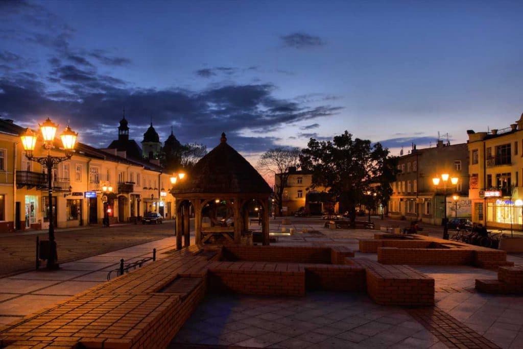 Rynek w Chełmie nocą — Plac Kupiecki z latarniami i sylwetką bazyliki w tle