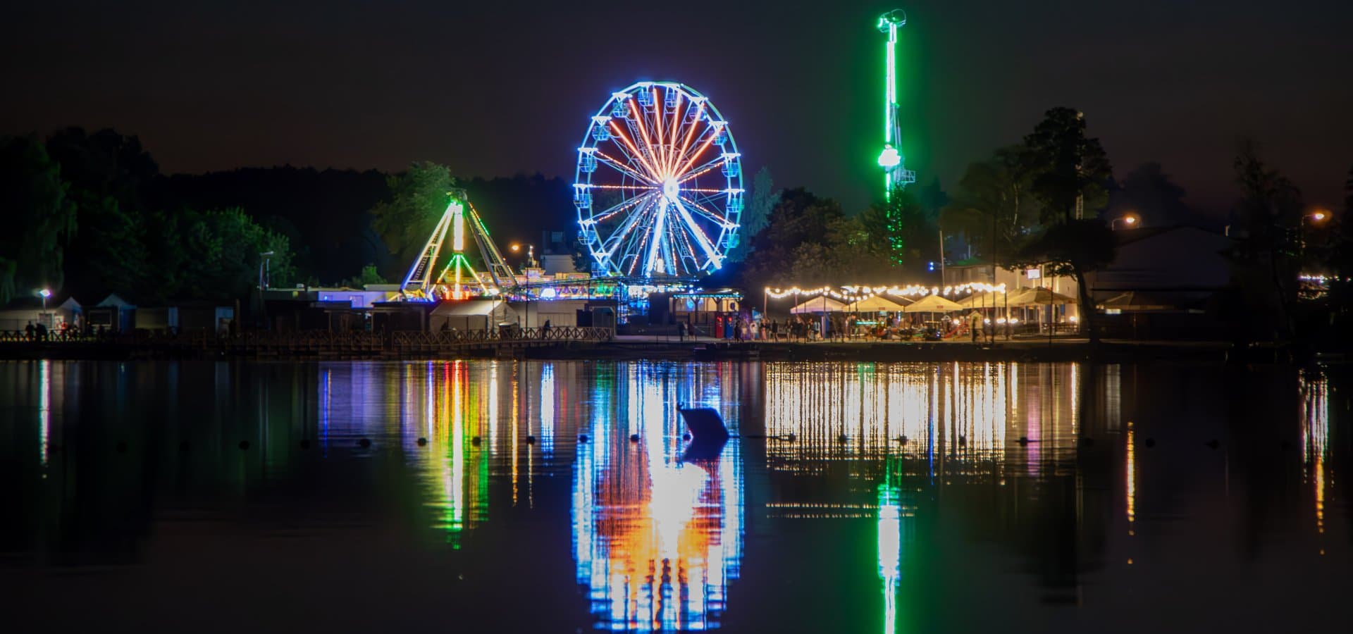 Lunapark w Okunince nocą — koło widokowe i atrakcje odbite w Jeziorze Białym