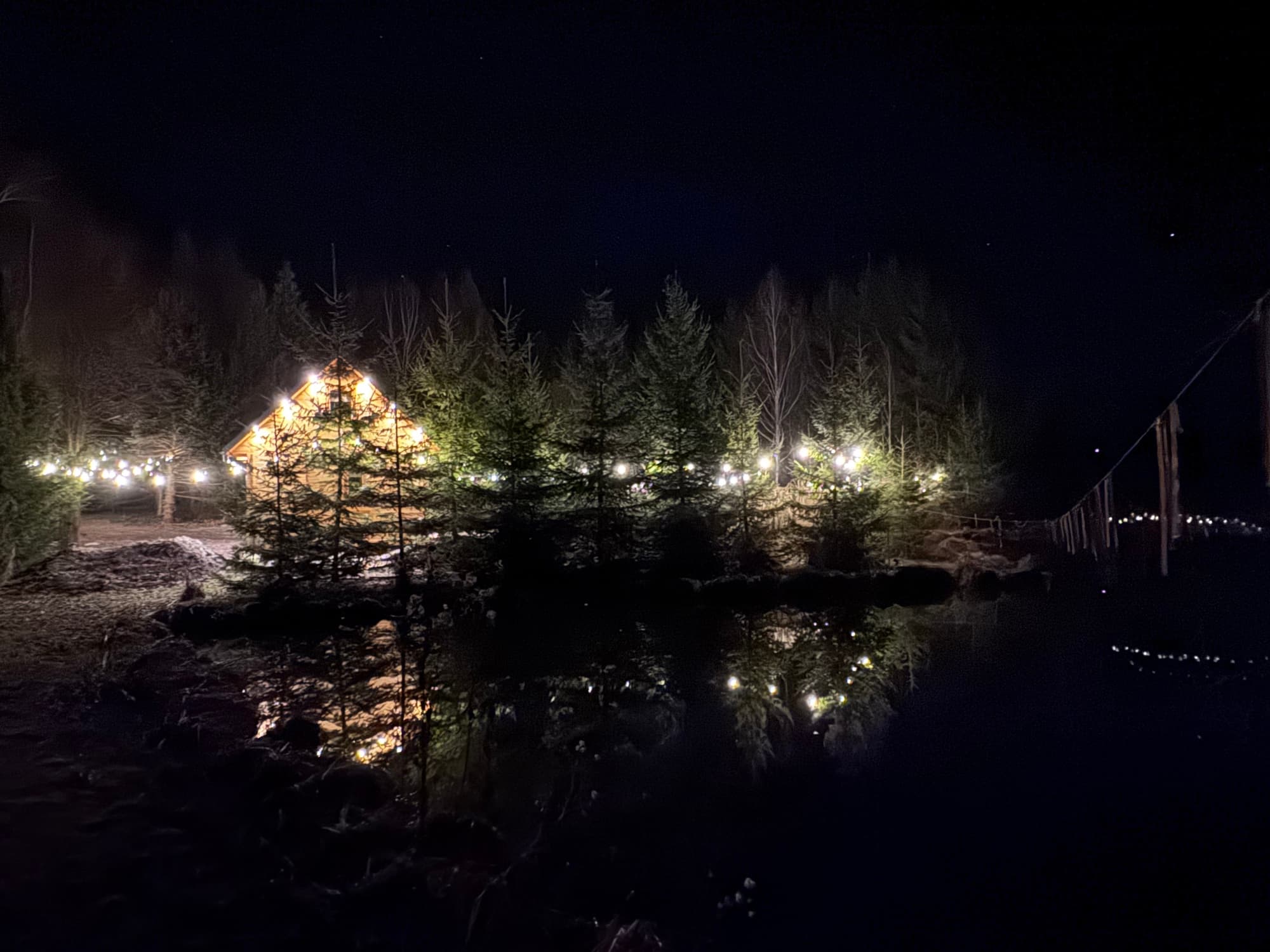 Domek nocą z girlandami swietlnymi odbijajacymi sie w stawie